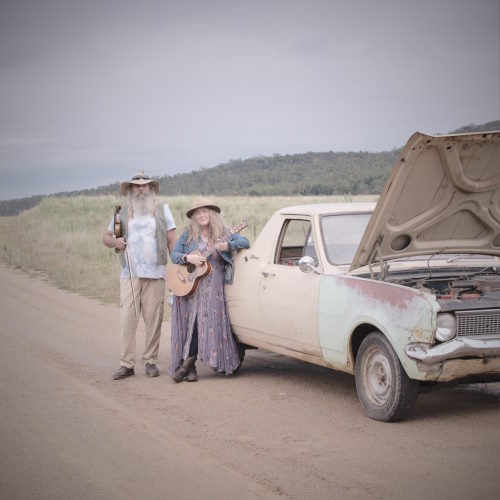 Frock and Troll Photo of two performers standing in front of dead car