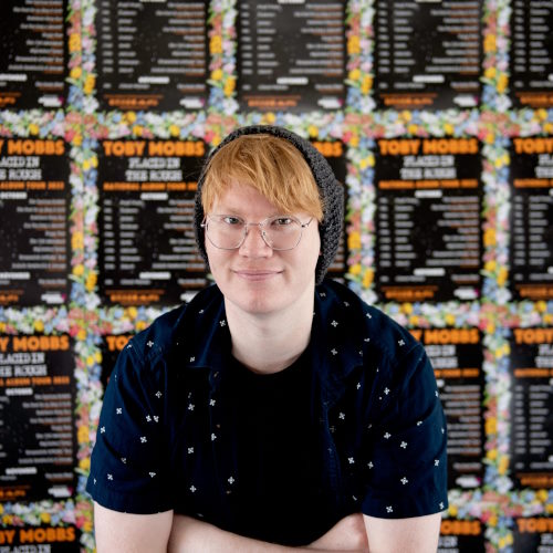 Toby Mobbs Toby Mobbs smiles from in front of his performance posters