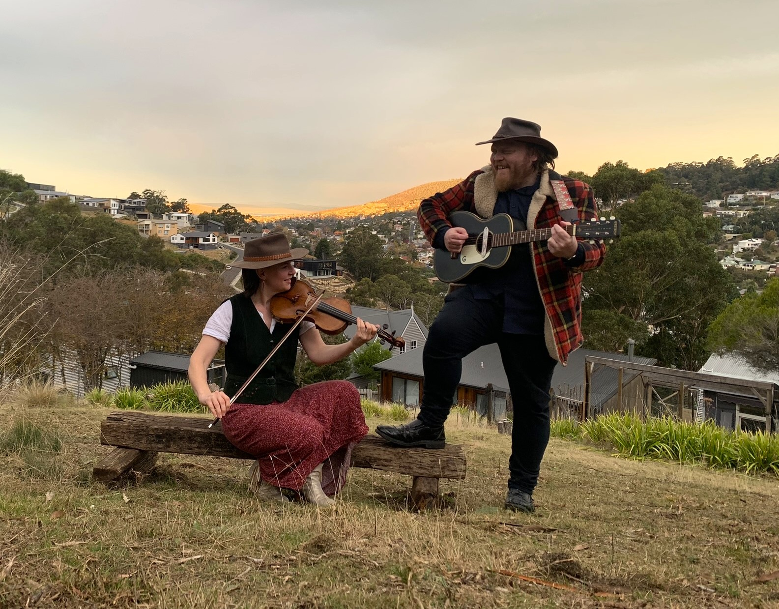 Wallaby Bush Duo Outdoor photograph of Susannah sitting playing violin and Dave standing playing guitar